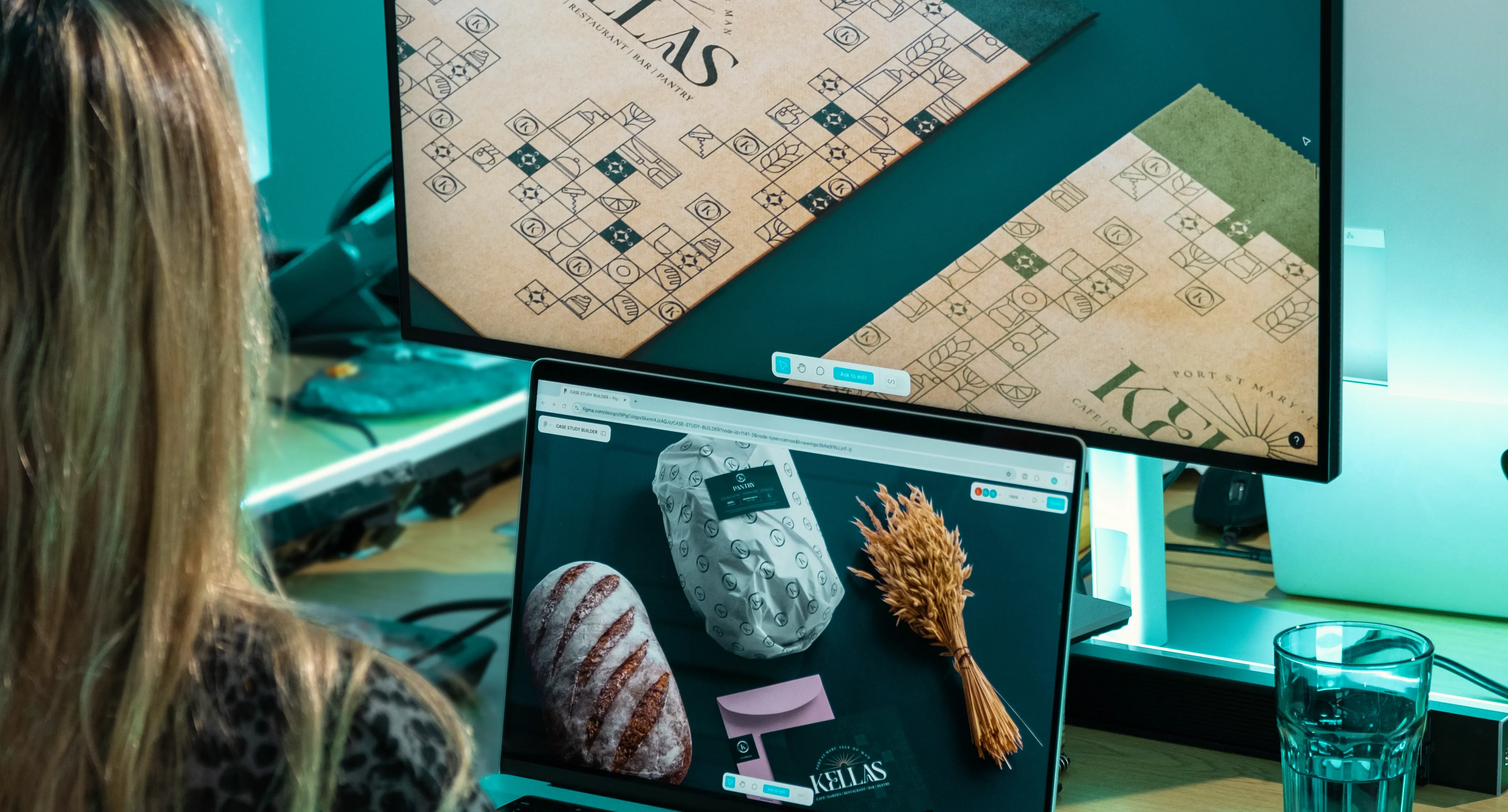 Rachel Fabrizio reviewing Kellas brand identity and collateral designs across two monitors at the DotPerformance studio on the Isle of Man